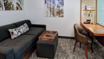 A modern living room with a grey sofa, a wooden coffee table, a small ottoman, a desk with a chair, and abstract wall art.