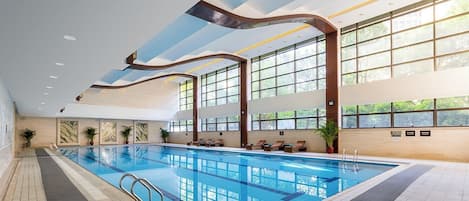 Una piscina interior con paredes de vidrio transparente, piso de baldosas y techo con un diseño ondulado original.