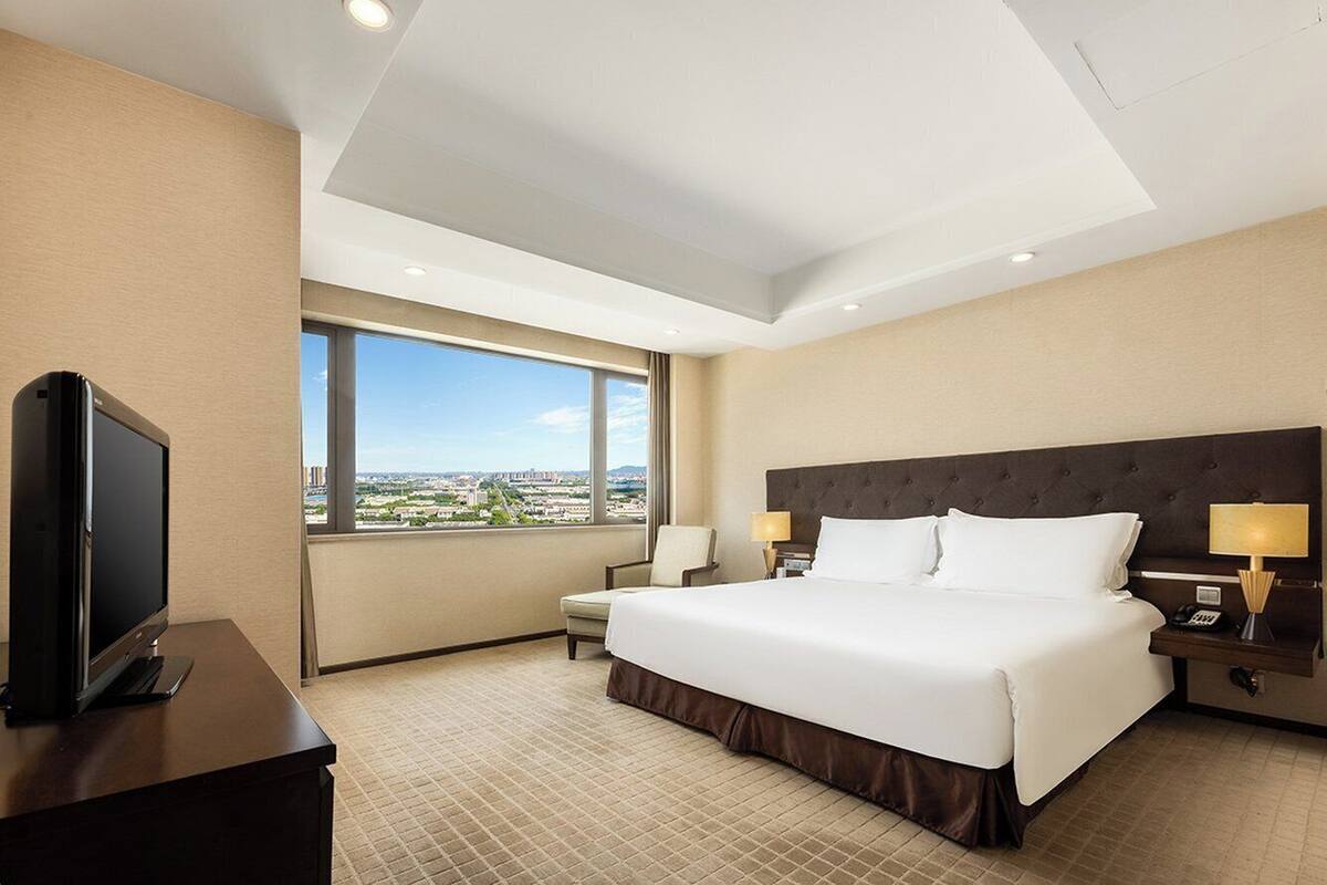 Une chambre d’hôtel avec un grand lit, une télévision, un fauteuil et une vue sur la ville.