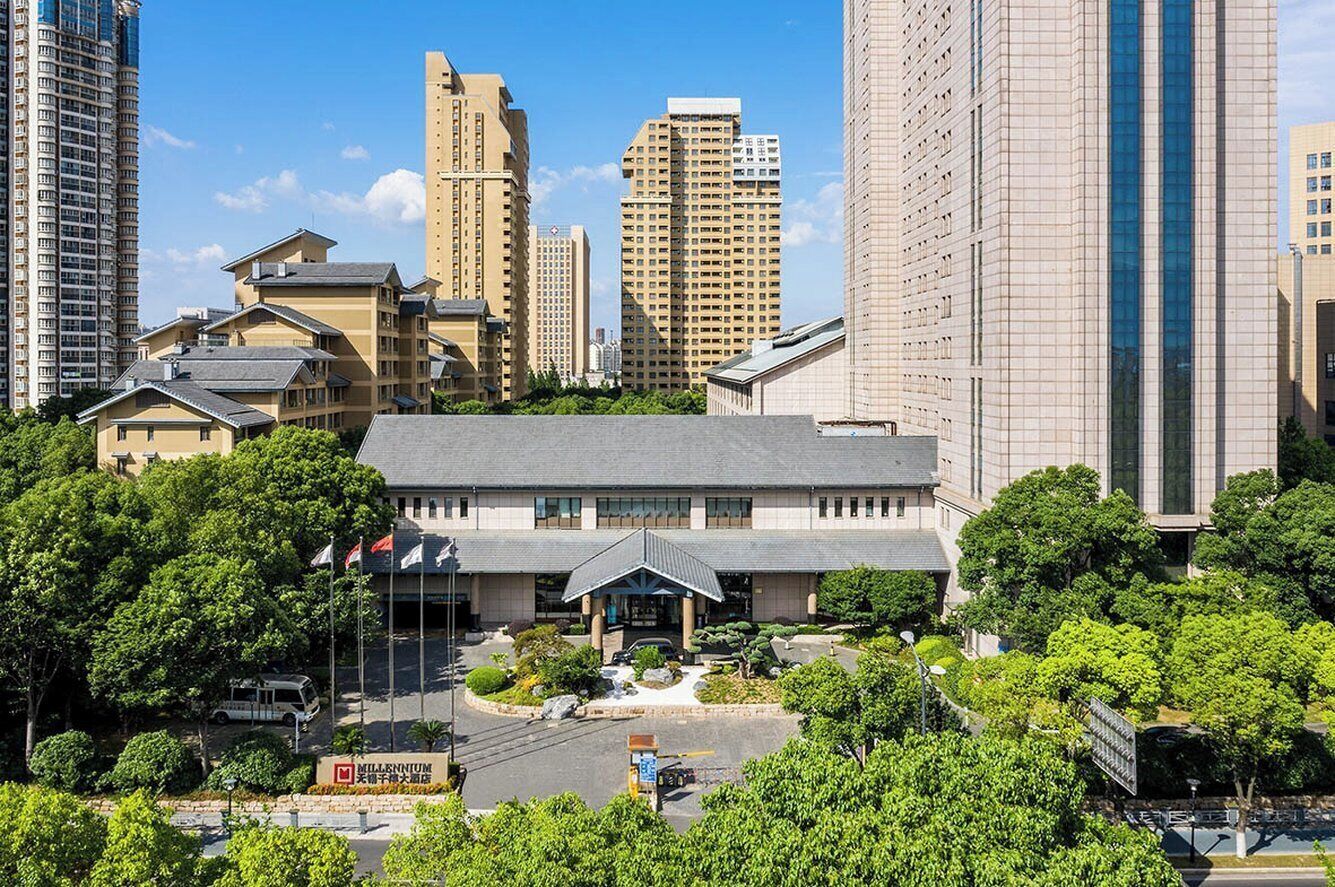 A hotel with a modern design, surrounded by tall buildings and lush greenery.
