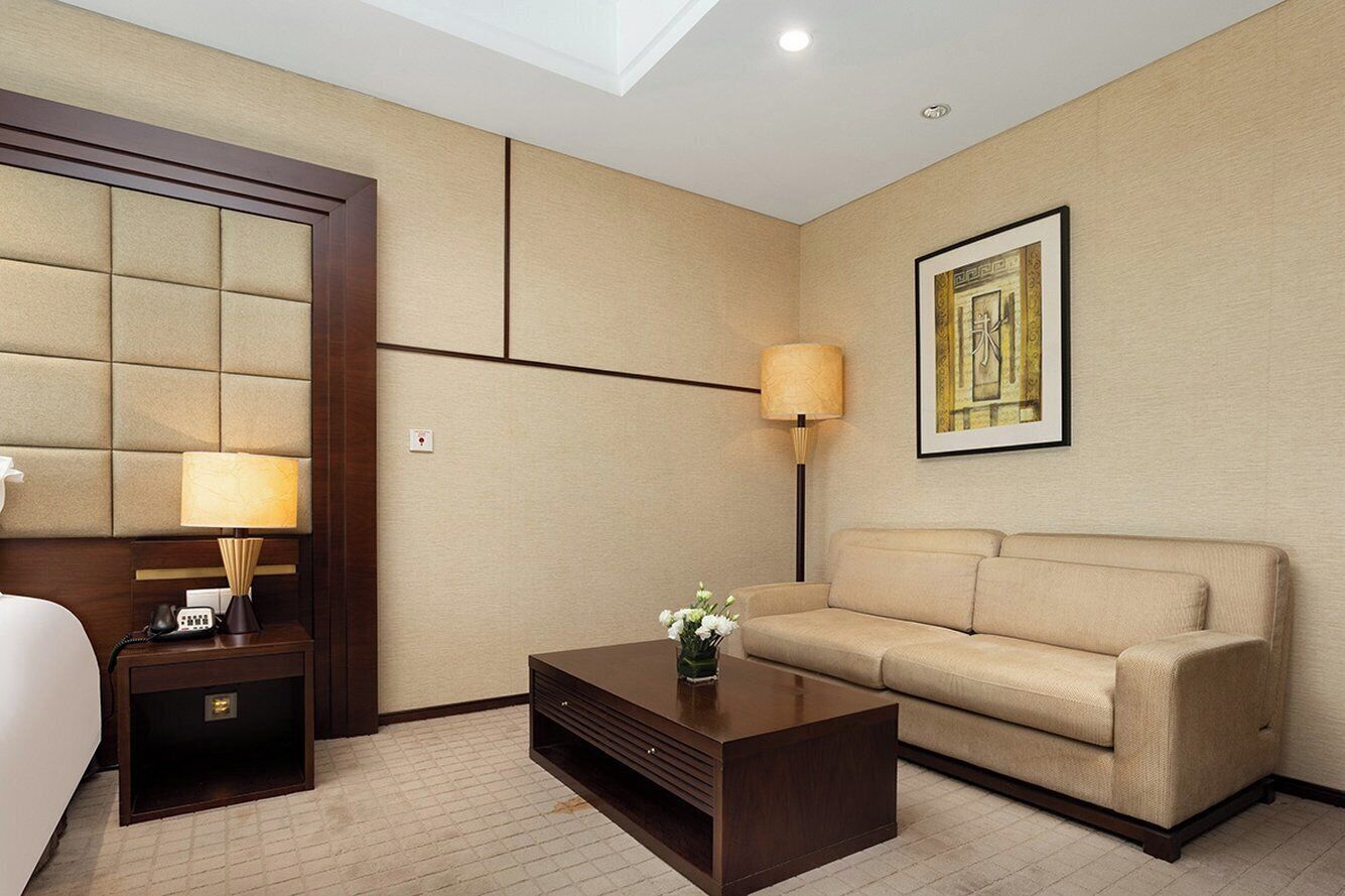 A hotel room with a bed, a nightstand with a lamp, a sofa, and a coffee table.