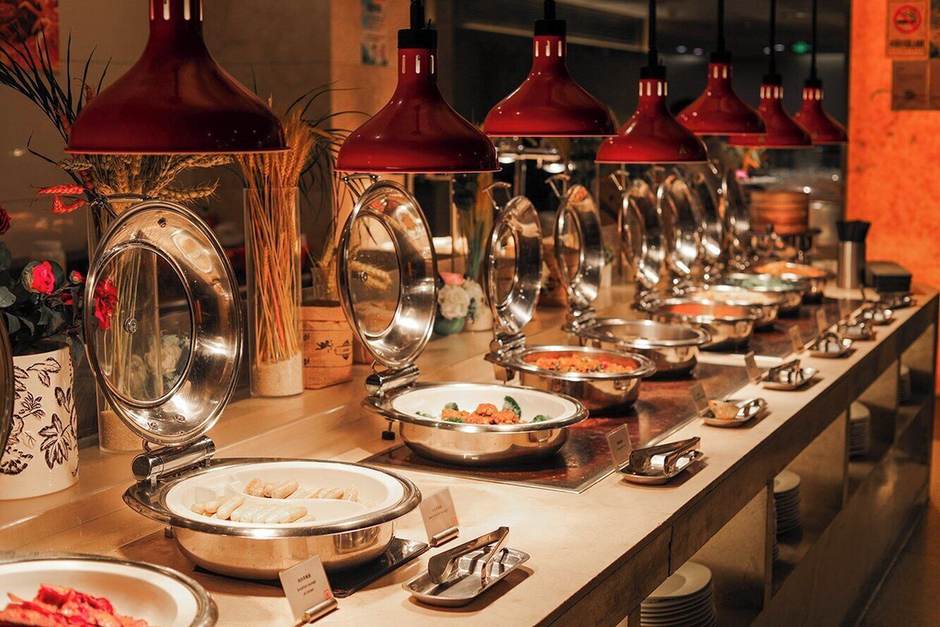 A buffet line with various dishes and utensils, including a decorative vase and a sign indicating the type of food.