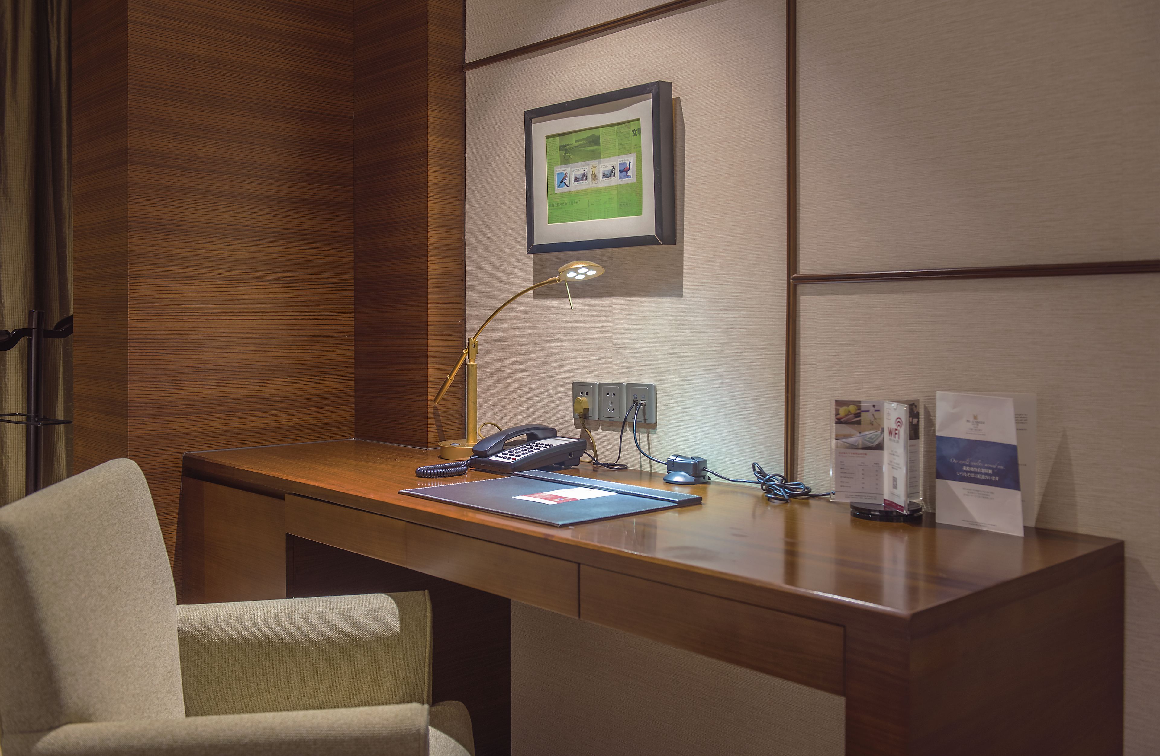 A wooden desk with a telephone, a lamp, and a framed picture on the wall.