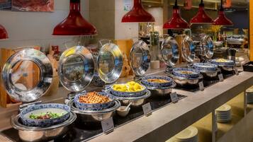 A buffet with various dishes in blue and white patterned bowls, red pendant lights, and a counter with stacked plates.