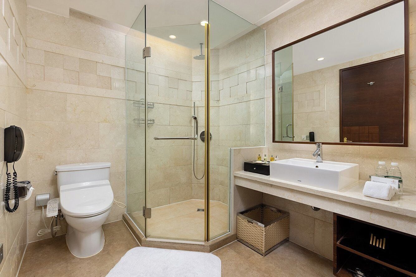 A modern bathroom with a glass-enclosed shower, a white toilet, a sink with a mirror above it, and a telephone on the wall.