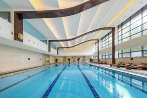 A large indoor swimming pool with clear blue water, surrounded by lounge chairs and potted plants. - Millennium Hotel Wuxi (Wuxi)