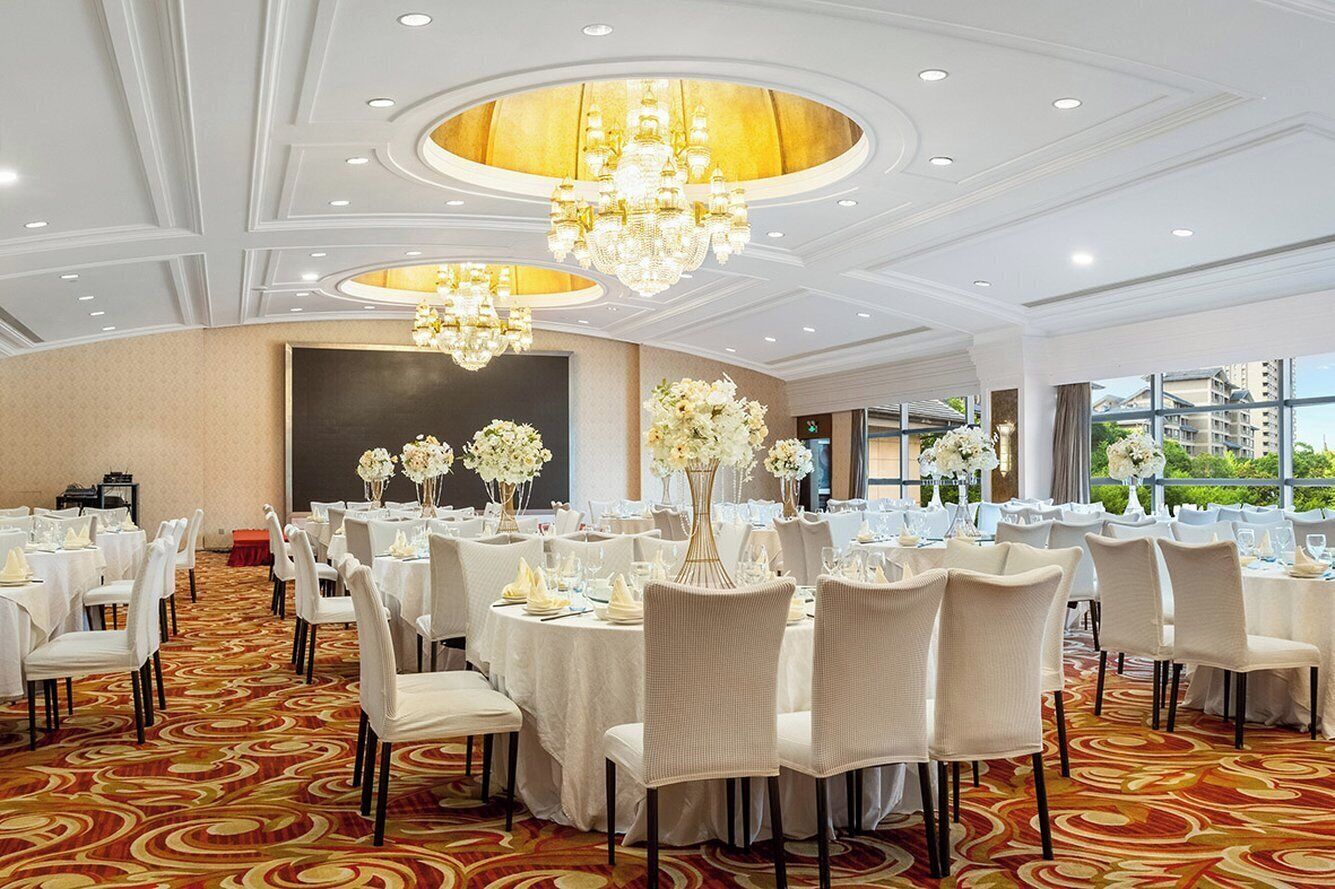 A banquet hall with round tables, white chairs, and chandeliers.