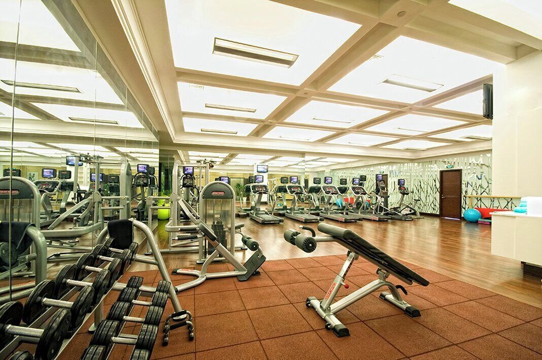 Un gimnasio amplio con diversos equipos de ejercicio, incluyendo cintas de correr, máquinas de pesas y pesas libres.