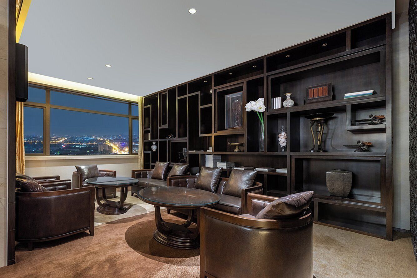 Un salon moderne avec des meubles en cuir, une grande fenêtre donnant sur la ville et des étagères intégrées ornées d’objets décoratifs.