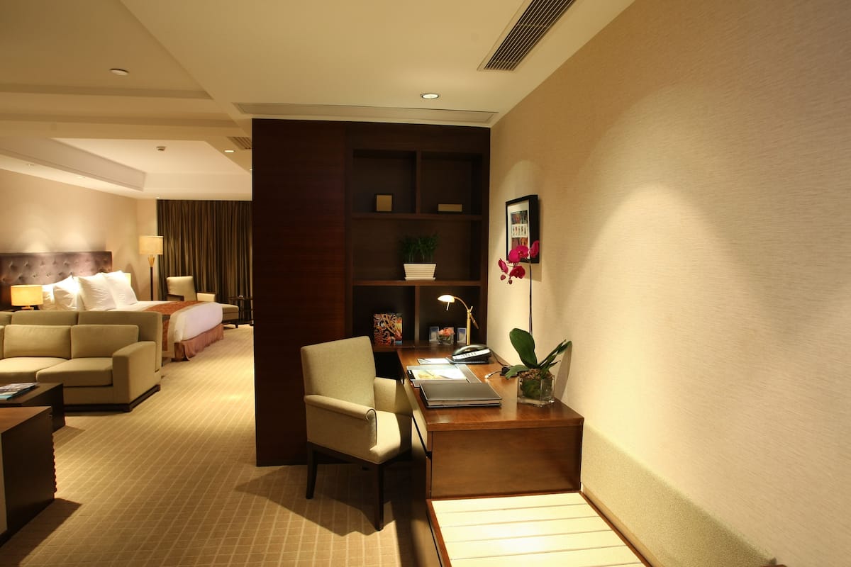 Une chambre d’hôtel comprenant un lit, un canapé, un bureau avec une lampe, une bibliothèque et une plante en pot.
