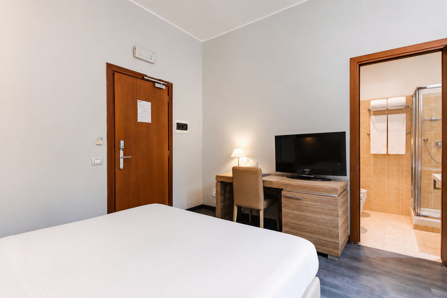 Een hotelkamer met een bed, een bureau met een televisie, een stoel en een douche.