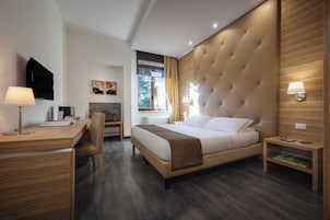 Una moderna camera d'hotel con un letto grande, una scrivania, una sedia, una televisione e una finestra con tende.