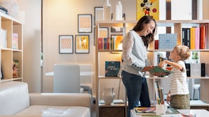A cozy living room with a white sofa, a bookshelf filled with books and decorative items, and a coffee table with books and a vase. - Phi Hotel Garden Area Roma Eur (Rome)