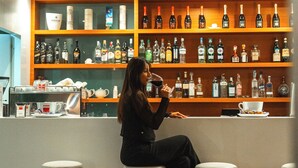 A woman sitting at a bar with shelves of bottles behind her. - Phi Hotel Garden Area Roma Eur (Rome)