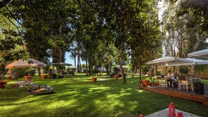 An outdoor patio area with seating, umbrellas, and potted plants. - Phi Hotel Garden Area Roma Eur (Rome)