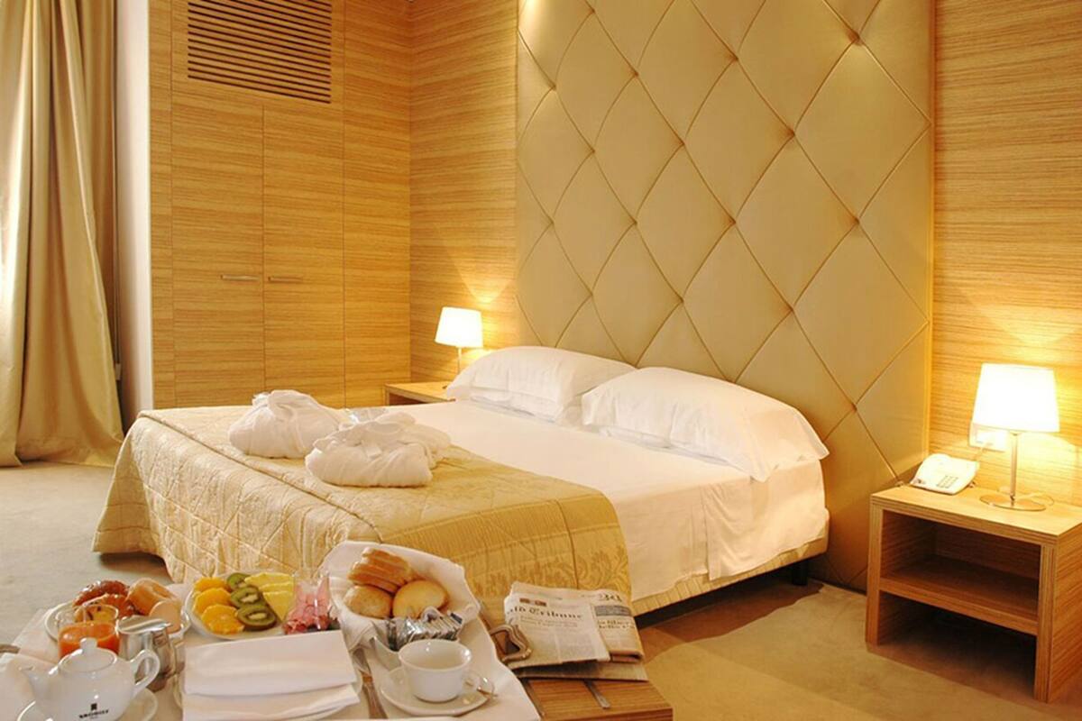 A hotel room with a large bed, two bedside lamps, a wooden headboard, and a breakfast tray with various items.