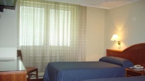 Habitación de hotel con dos camas, un escritorio, una silla y un ventanal con cortinas traslúcidas.