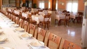 Una larga mesa de comedor dispuesta con manteles blancos y sillas, en una habitación con paredes color crema y vigas de madera.