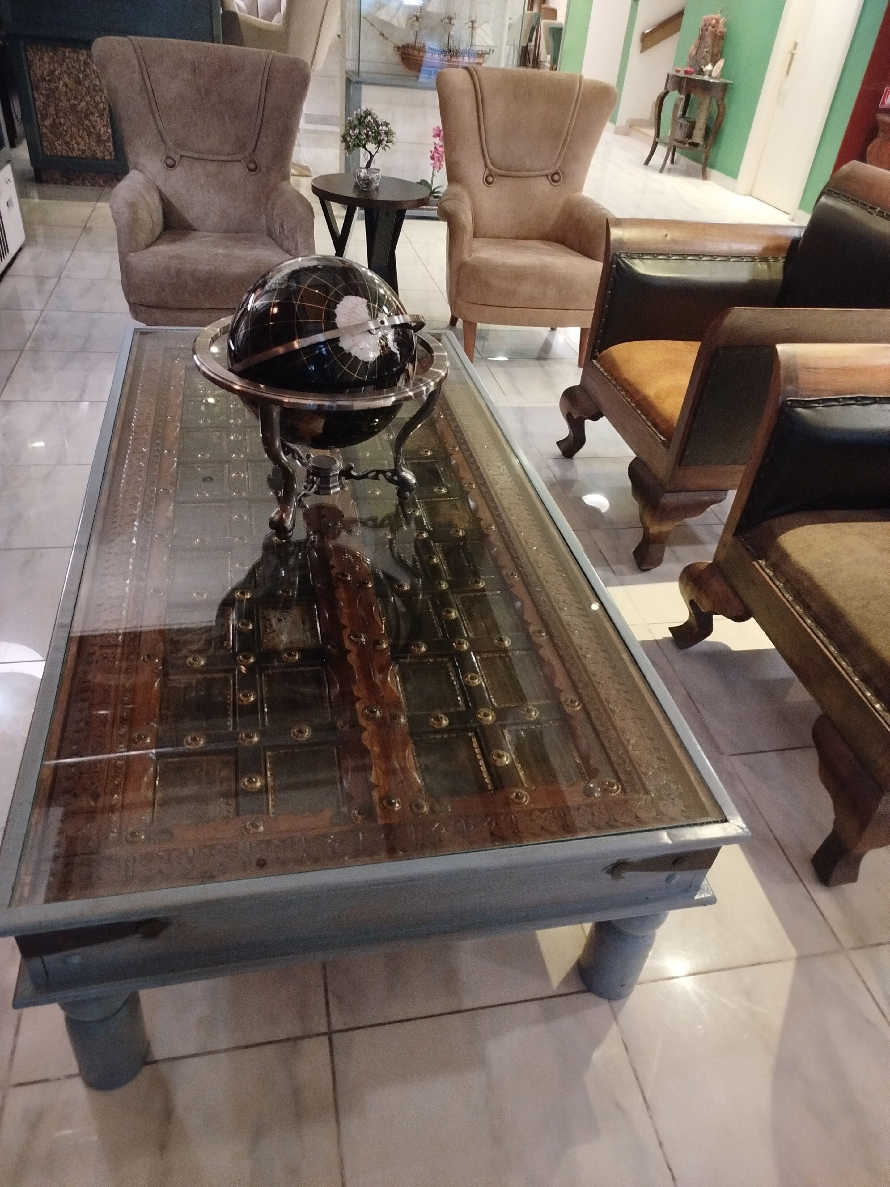 A room with a glass-top coffee table, two armchairs, and a small side table with a vase.