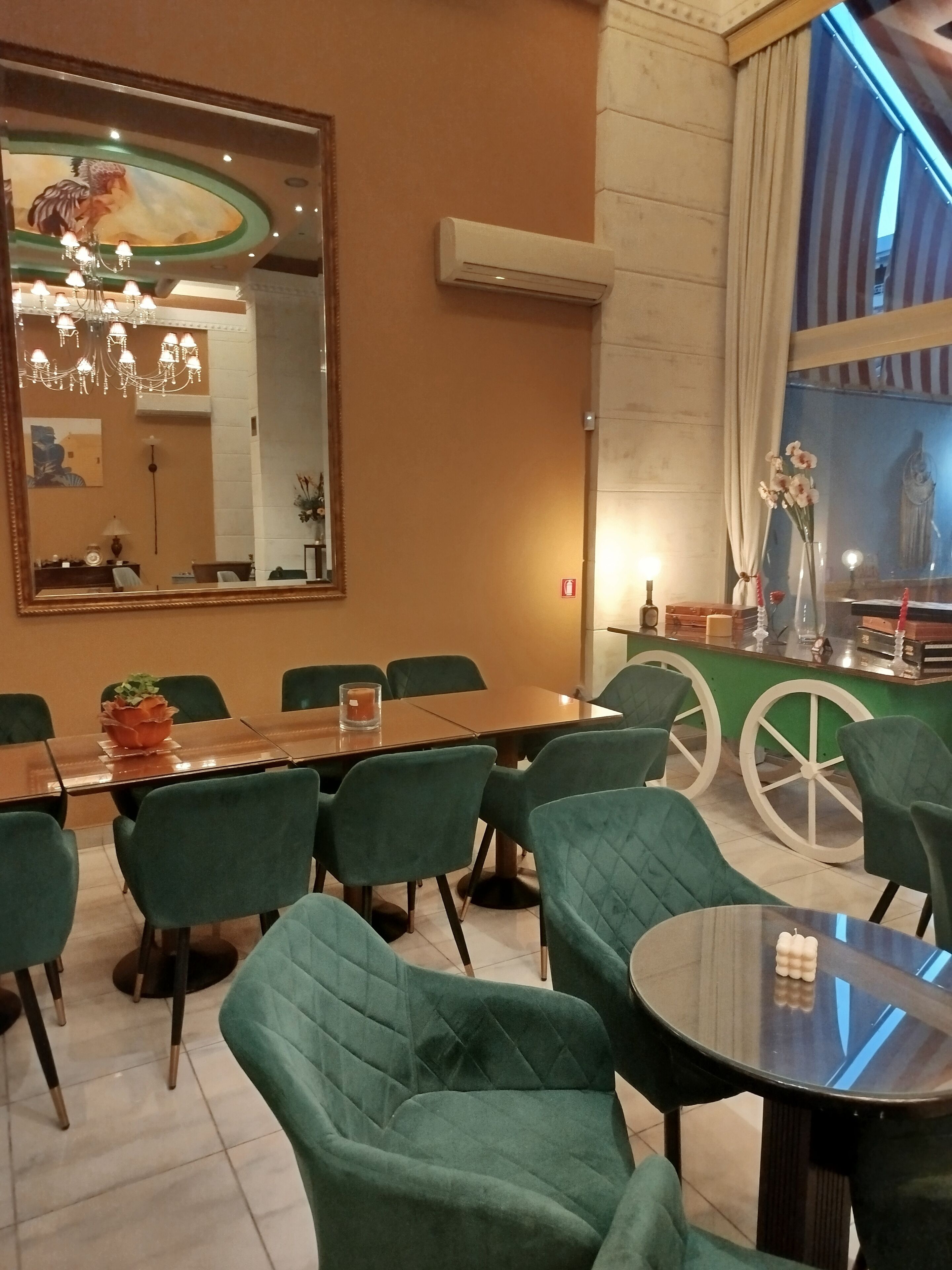 A dining area with a large mirror, green chairs, a wooden table, and a chandelier.
