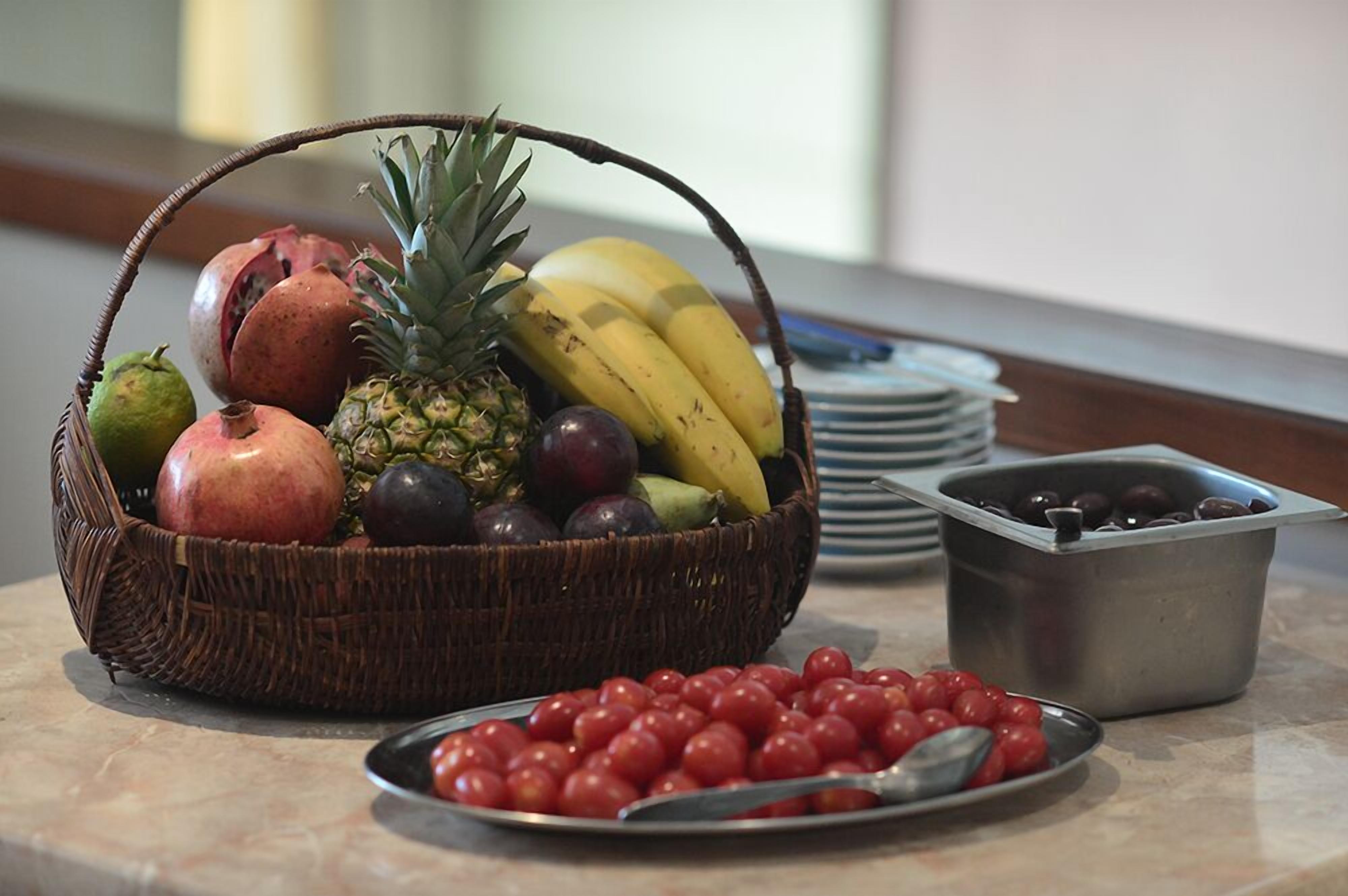 A fruit basket with bananas, pineapple, and pomegranate on a marble countertop.