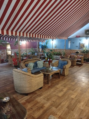 A covered outdoor seating area with wicker furniture, a wooden floor, and potted plants. - Ephira Hotel (Corinth)