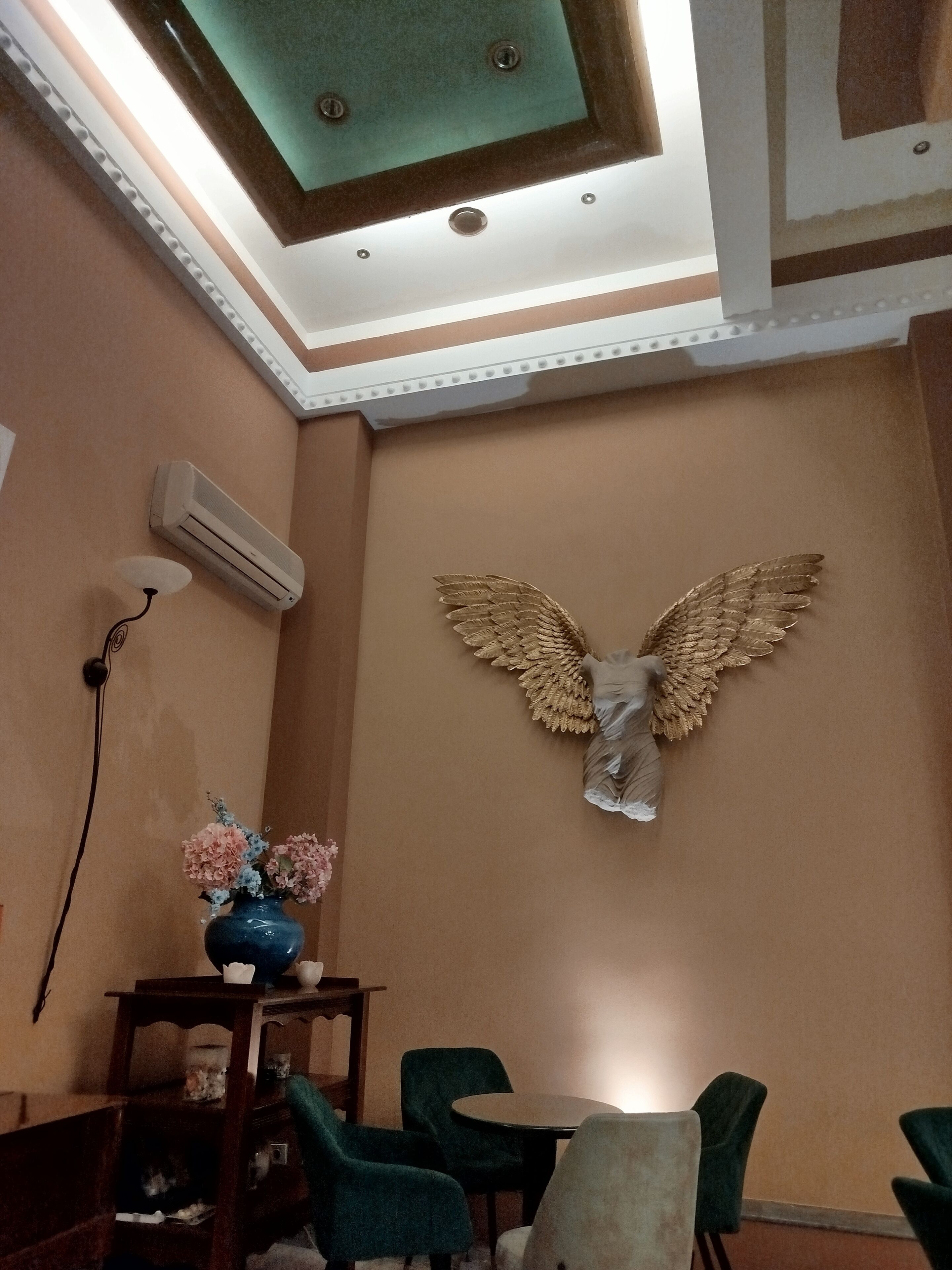 A room with a dining table, chairs, an air conditioning unit, and a decorative angel on the wall.