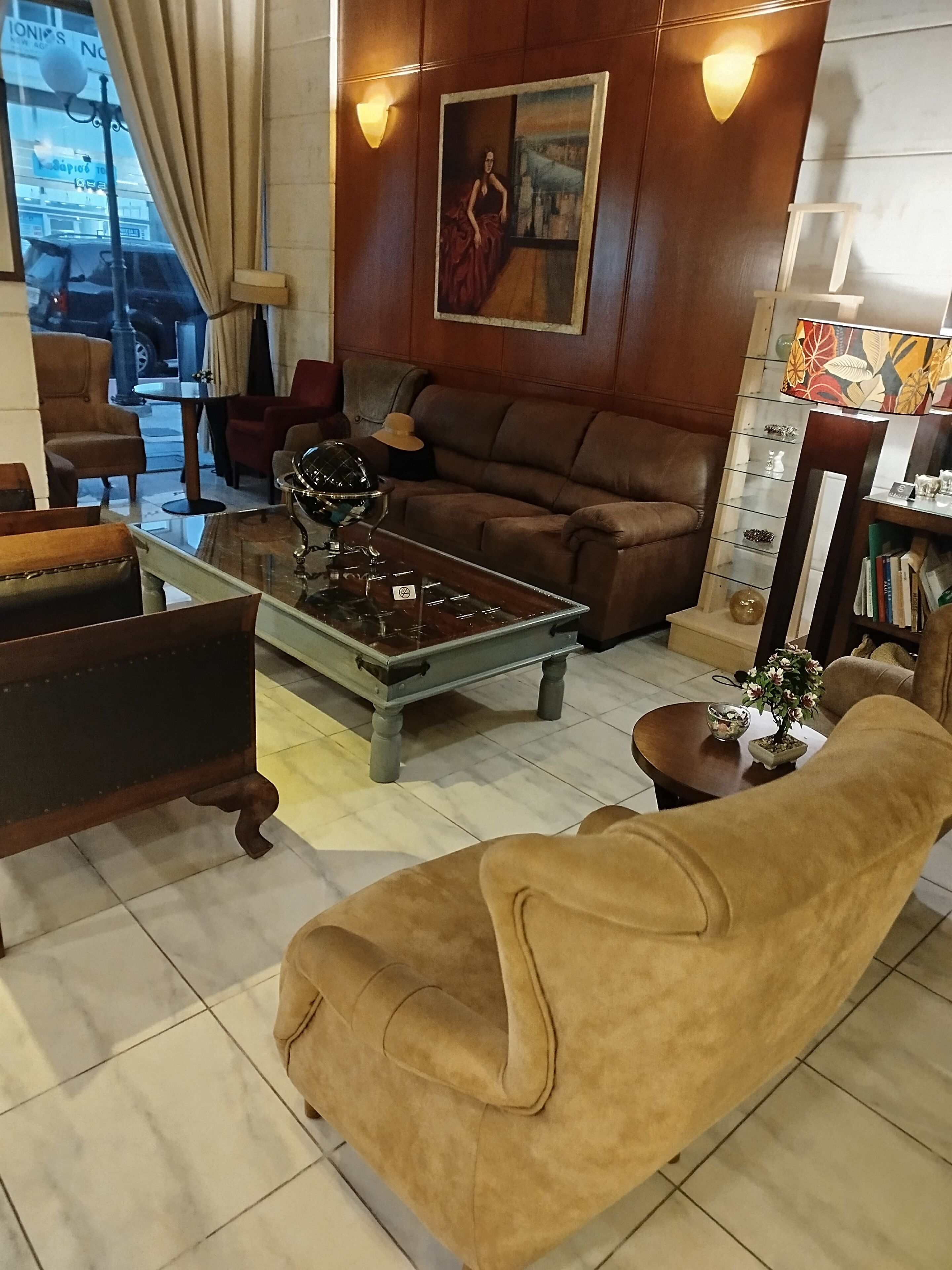 A living room with a brown sofa, a glass coffee table, a lamp, a painting on the wall, and a bookshelf.