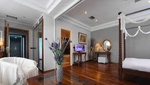 Une chambre d’hôtel comprenant un lit, un coin salon avec un fauteuil et une table, un téléviseur et un vase décoratif avec des fleurs.