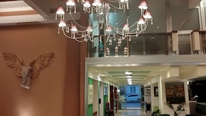 Un hall d’hôtel agrémenté d’un lustre, d’œuvres d’art au plafond et de fauteuils recouverts d’un tissu vert.