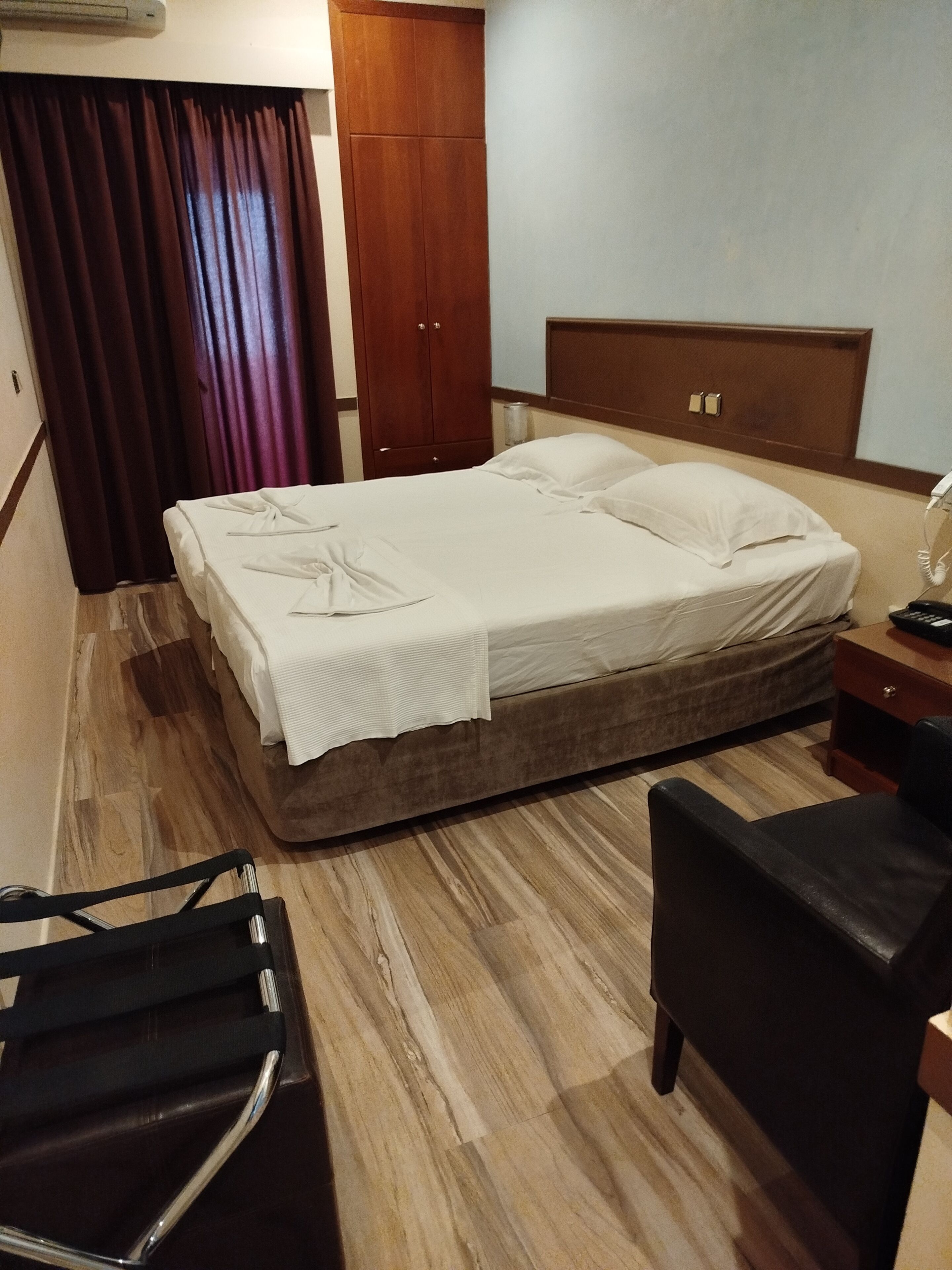 Une chambre d’hôtel comprenant un lit, une armoire en bois, un bureau avec une chaise et un téléphone.