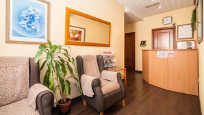 A reception area with a wooden desk, a framed artwork, a potted plant, and a patterned sofa. - Hostal Gallardo (Madrid)