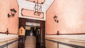 A grand staircase with ornate railings and wall sconces, leading to a reception area with a signboard. - Hostal Gallardo (Madrid)