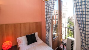 A bedroom with a wooden headboard, a bed with white bedding, a black pillow, and a window with checkered curtains. - Hostal Gallardo (Madrid)