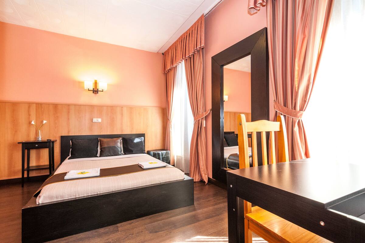 A hotel room with a wooden bed, a nightstand, a mirror, and a wooden chair.