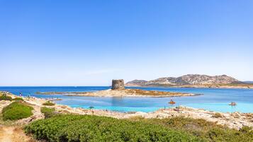 A coastal landscape with a clear blue sea, rocky terrain, and a small tower structure.