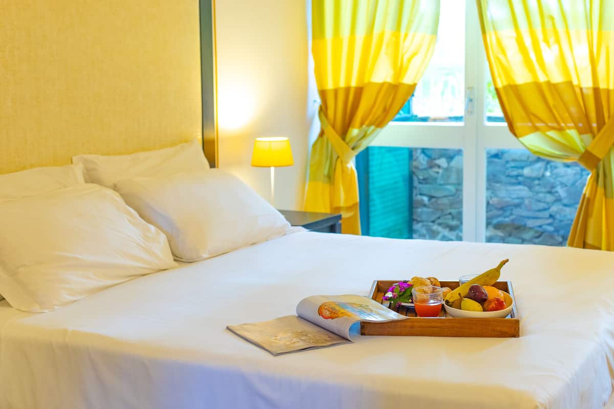 A neatly made bed with white linens, a tray of breakfast including fruits, a drink, and a magazine.