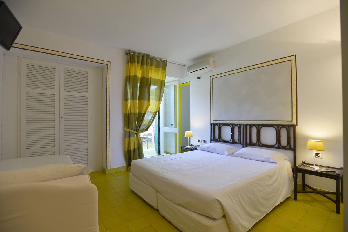 A hotel room with a large bed, two bedside tables with lamps, a wardrobe, and a view of the outside.