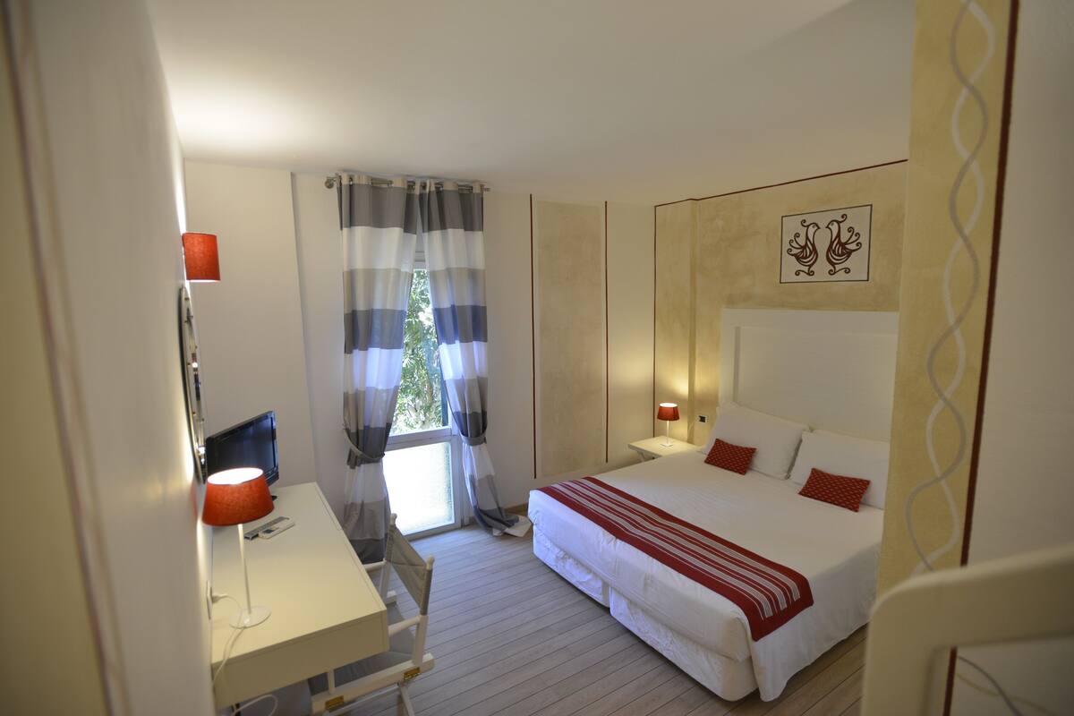 A hotel room with a bed, bedside table, lamp, and a window with curtains.