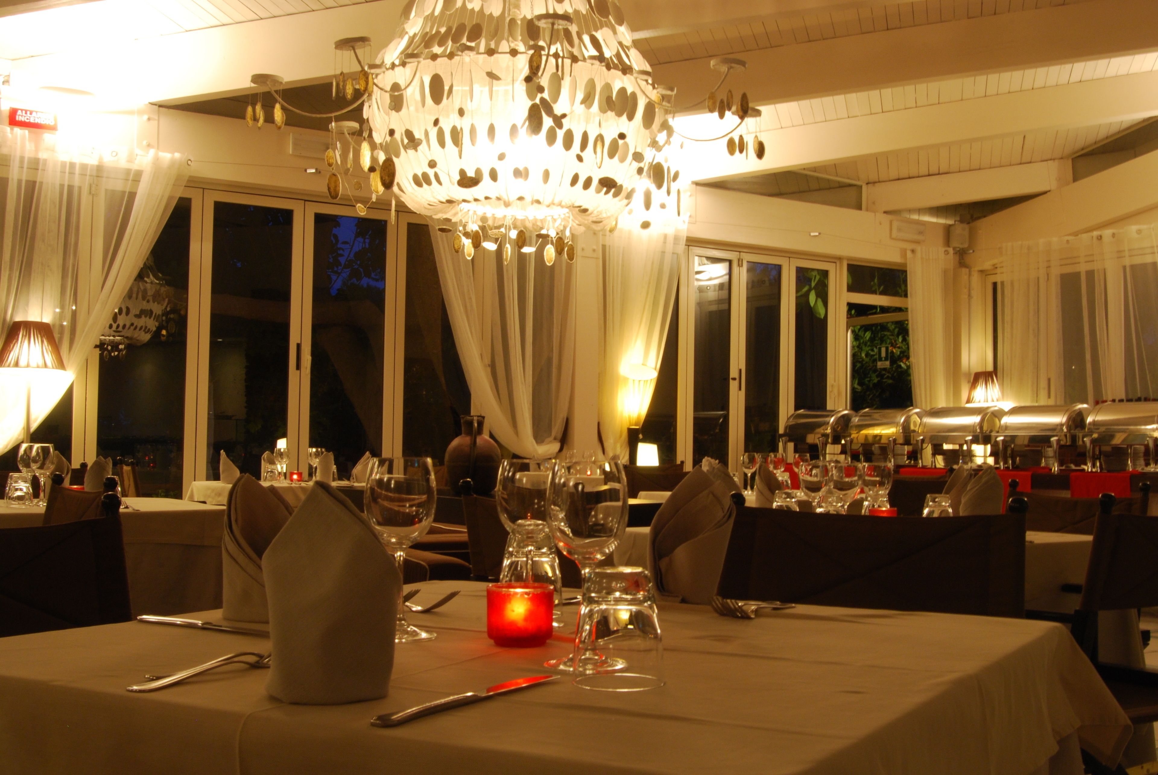 A dining area with tables set for a meal, a chandelier, and large windows.