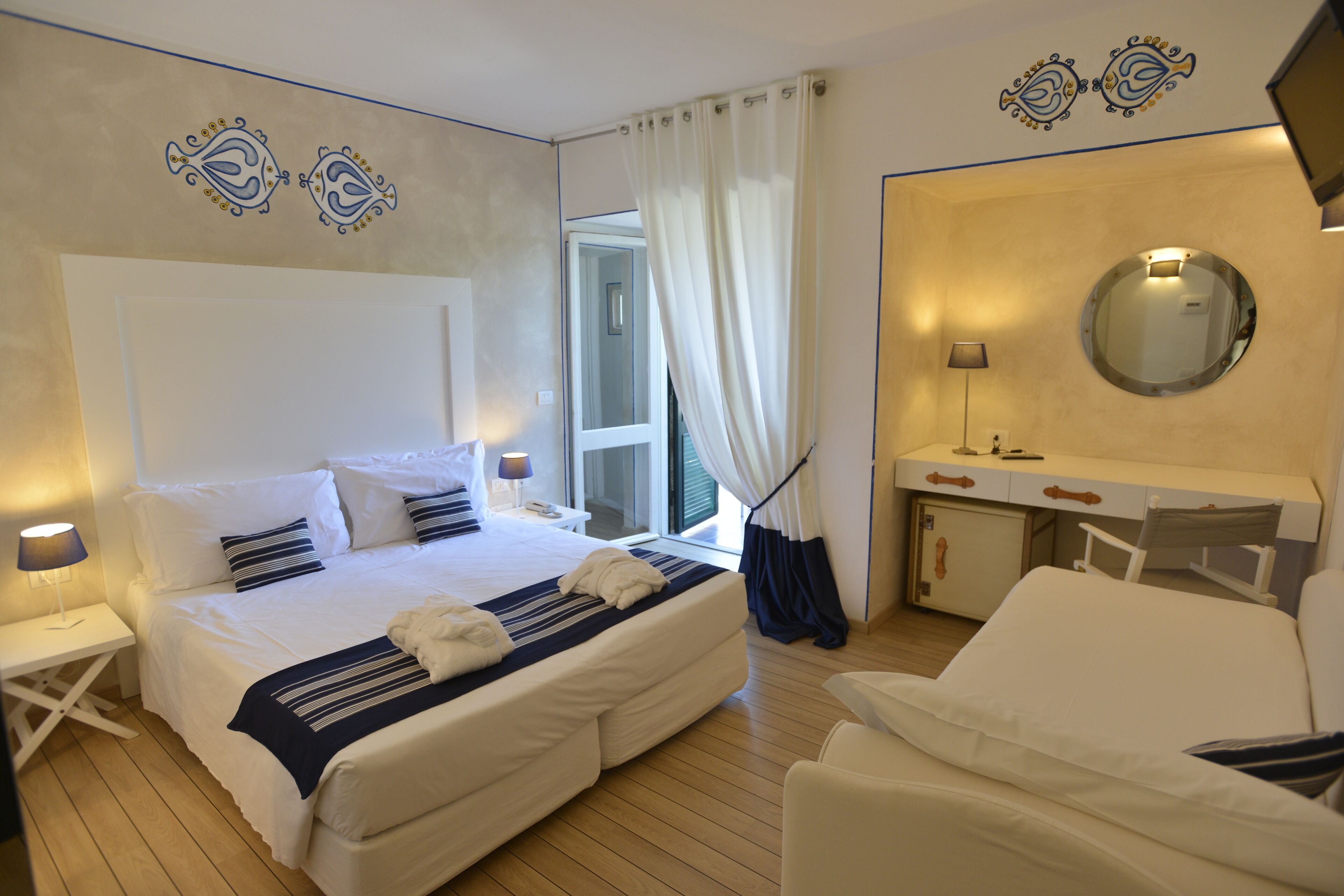 Une chambre d’hôtel avec un grand lit, un bureau, une chaise, un miroir et une fenêtre avec des rideaux.