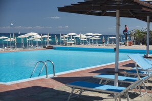 A pool area with lounge chairs and umbrellas, a lifeguard on a chair, and a view of the ocean.