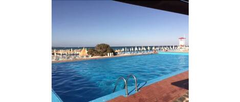 A swimming pool with a view of the sea and beach umbrellas.