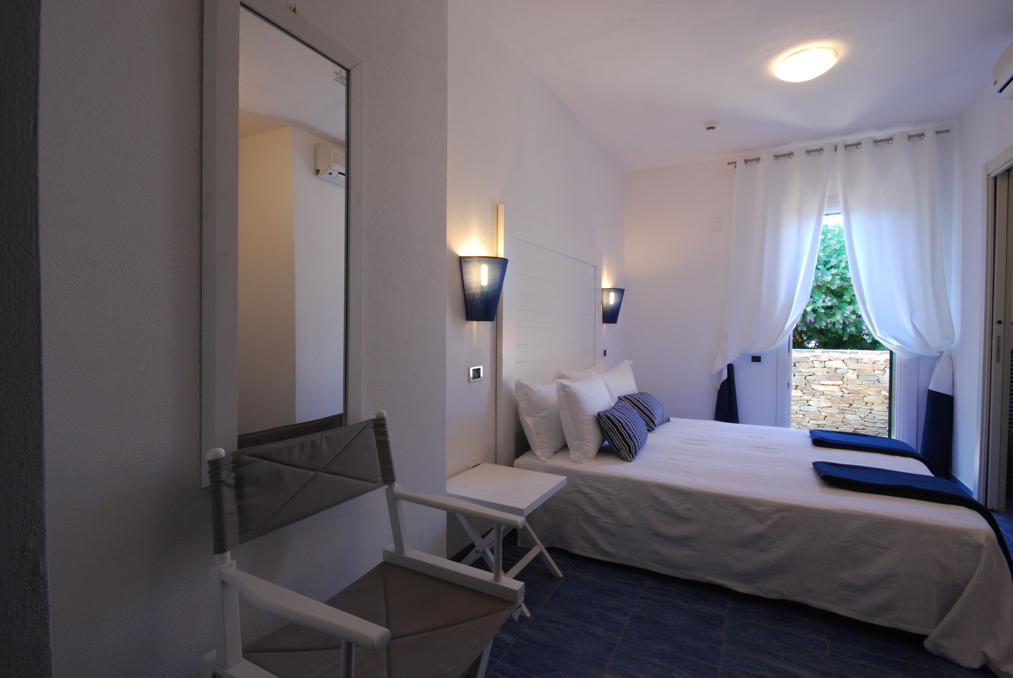 Une chambre à coucher comprenant un lit, une chaise, un miroir et deux lampes fixées au mur.