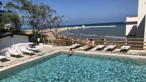 Ein Swimmingpool mit klarem Wasser, umgeben von Liegestühlen und Blick auf das Meer.