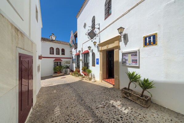 Una estrecha calle empedrada con edificios blancos, una puerta roja y plantas en macetas.