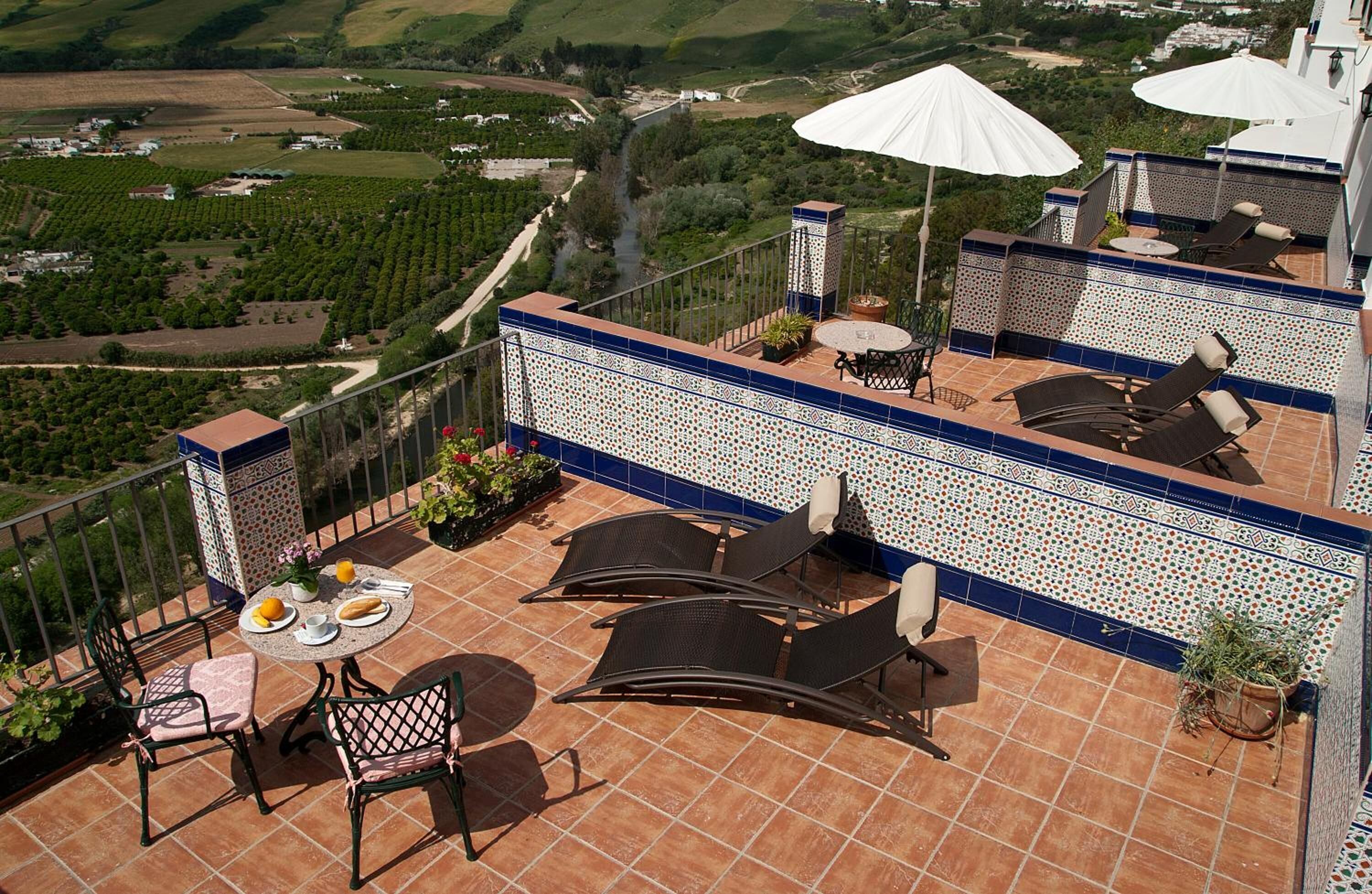 A rooftop terrace with outdoor seating, a view of vineyards, and a decorative tiled wall.