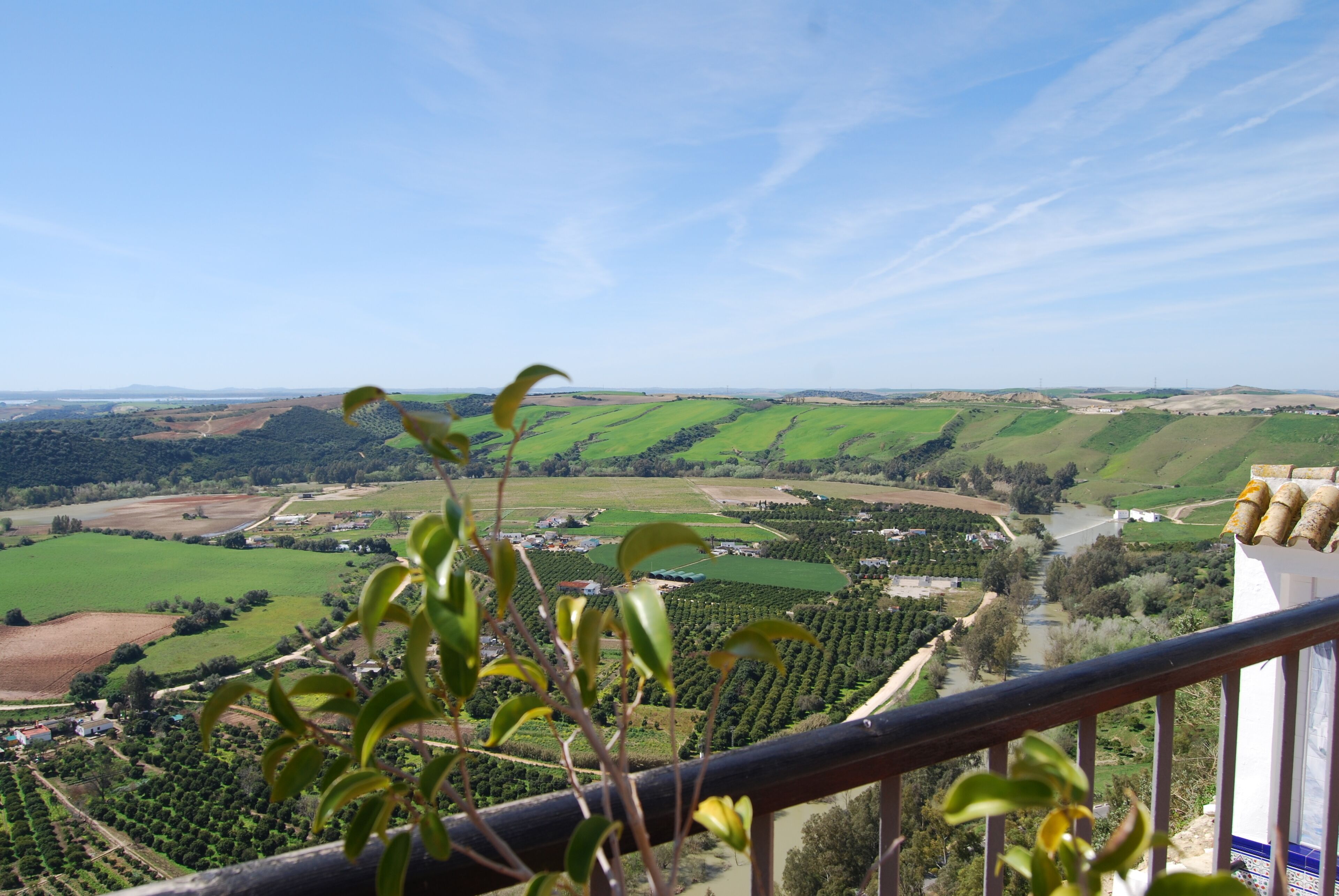 A balcony with a view of a green valley, a river, and distant hills.