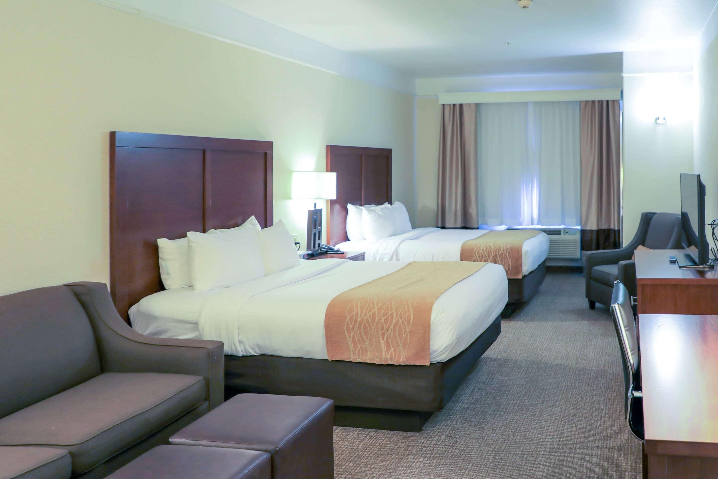 A hotel room with two beds, a desk, a chair, and a sofa.