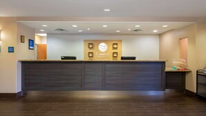 A reception desk with a sign reading "Comfort Inn & Suites," a dark wood floor, and a counter with a light-colored top. - Comfort Inn & Suites, Odessa I-20 (Odessa)